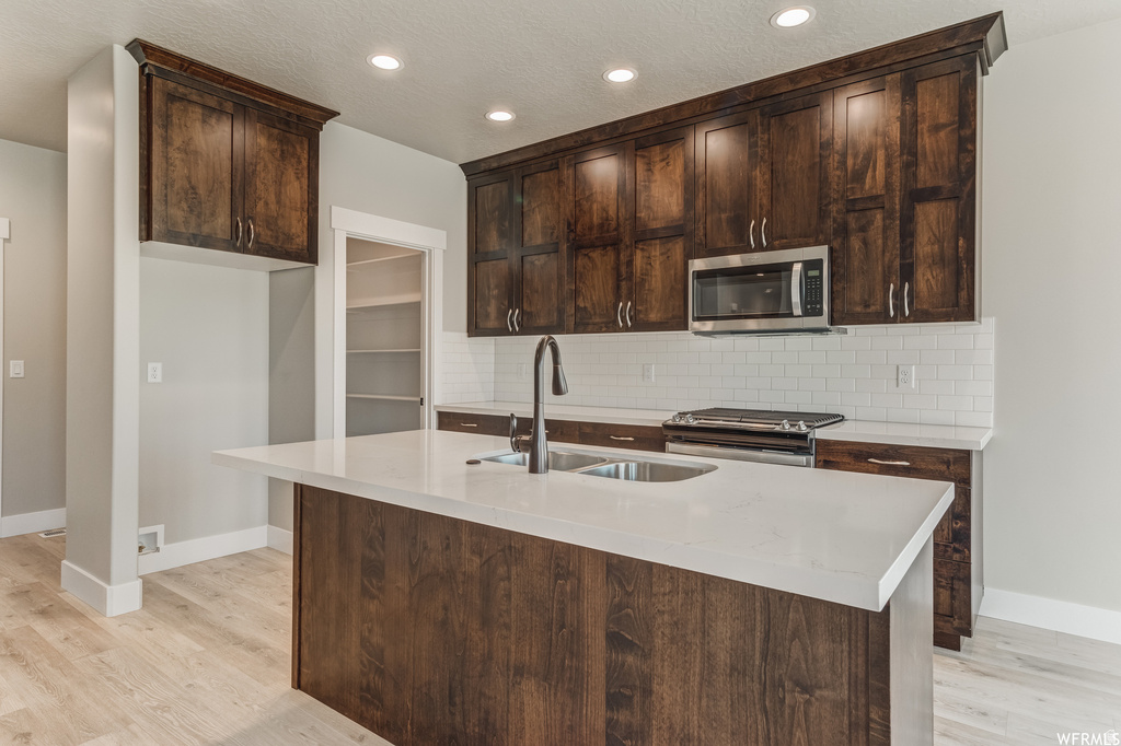 Spacious kitchen featuring dark wood-finish cabinetry, a large kitchen island with a sink, white countertop surfaces, a stainless steel microwave, and a white subway tile backsplash