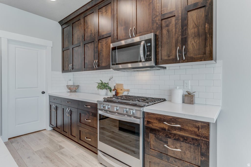 Kitchen featuring dark wood cabinetry, light countertops, white subway tile backsplash, stainless steel range with gas cooktop, and an over-the-range microwave