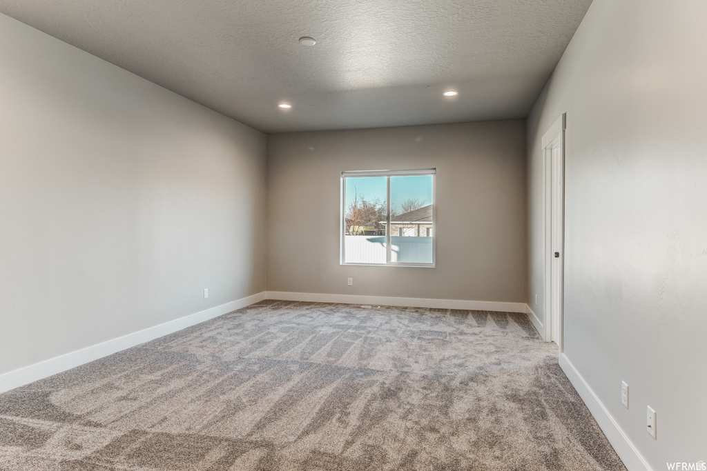Recessed lighting, neutral wall paint, gray patterned carpeting, white trim, and a bright window