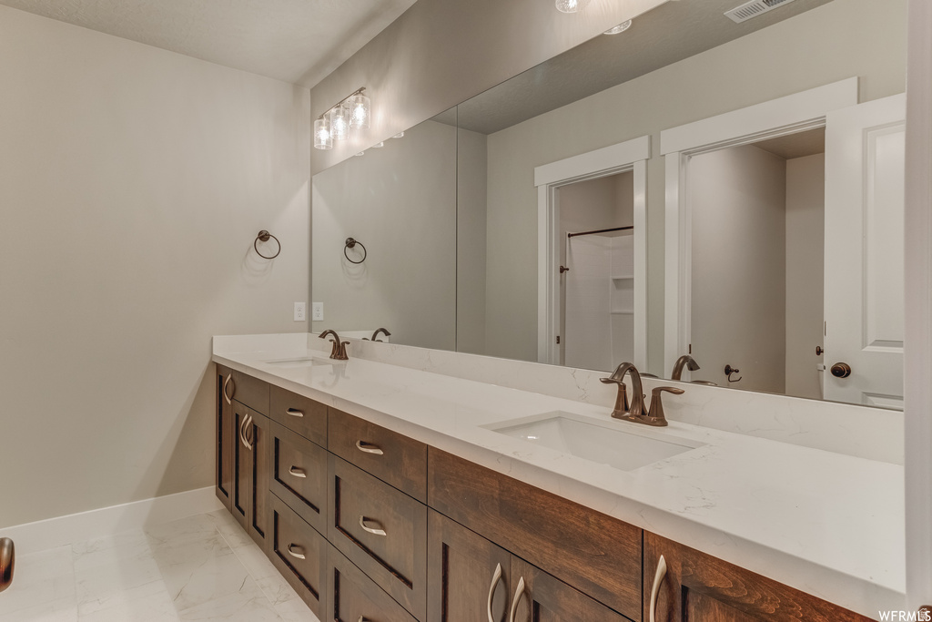 Dual vanity with integrated sinks, expansive mirror, wood-finish cabinetry, and contemporary bronze fixtures