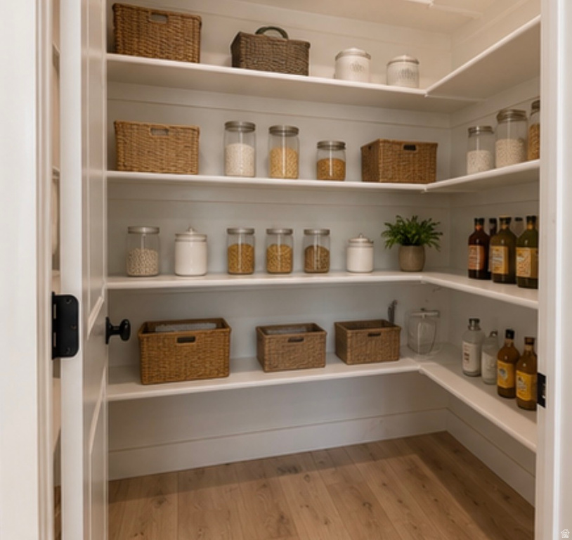 Walk-in pantry with light wood-finish flooring, extensive built-in shelving, and a white paneled door