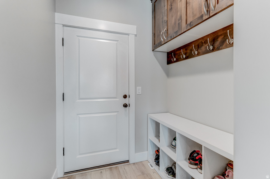 Entryway featuring wood-finish flooring, a paneled white door, built-in white cubby storage, a wood-finish wall-mounted coat rack, and dark wood cabinetry