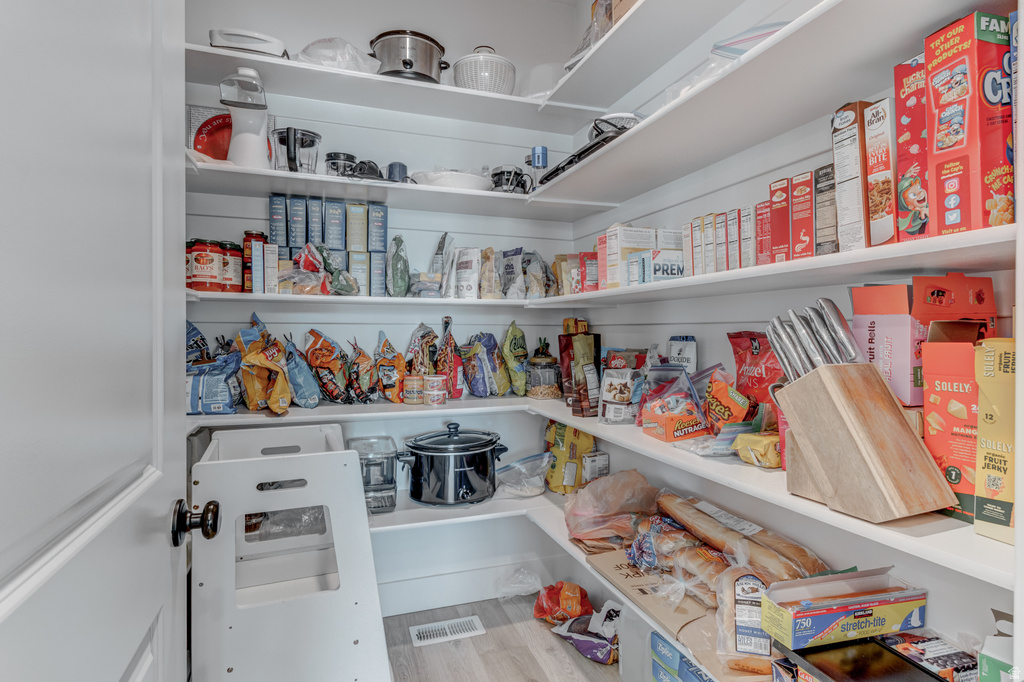 Walk-in pantry featuring extensive white shelving, wood-finish flooring, and ample storage space