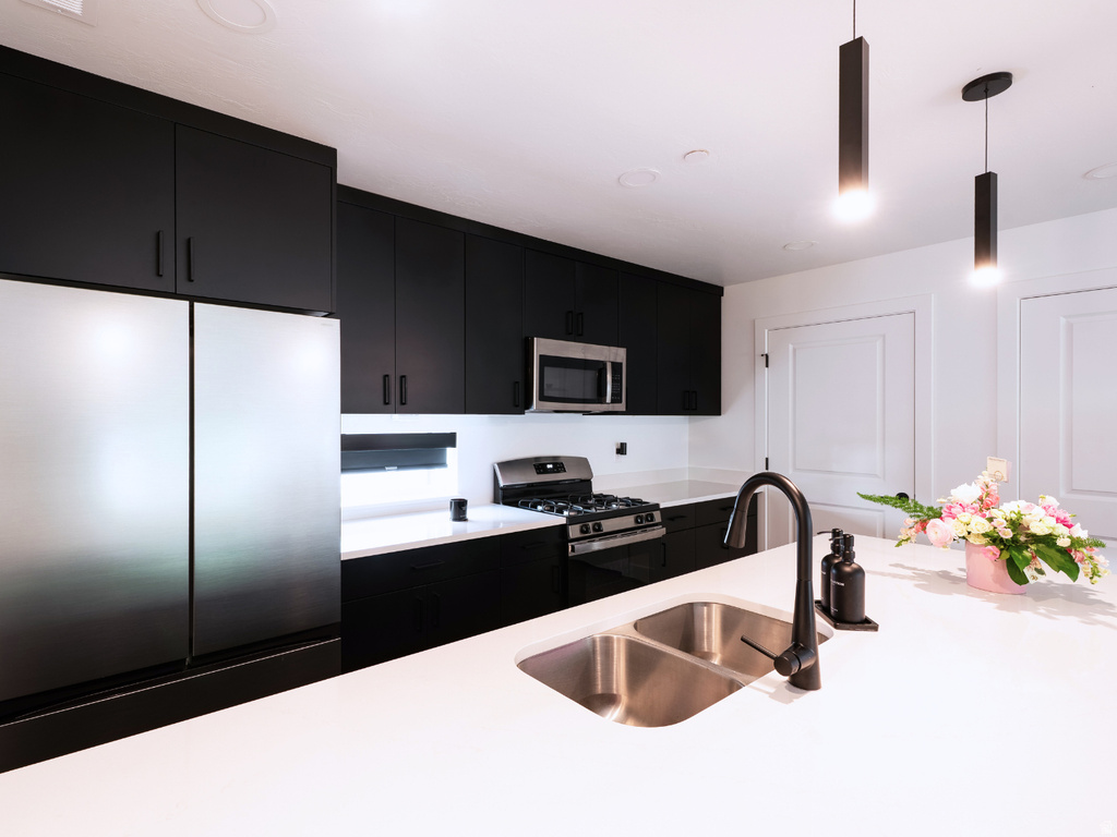 Contemporary kitchen featuring stainless steel appliances, black flat-panel cabinetry, white countertops, a dual basin sink with a matte black faucet, and pendant lighting