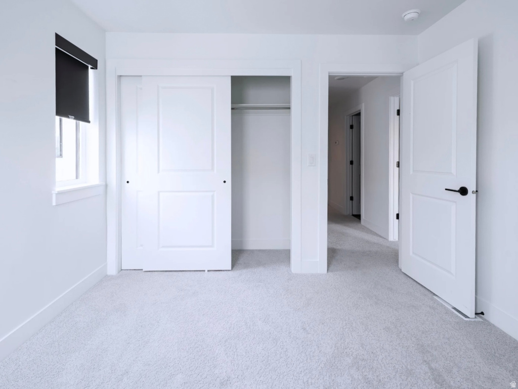 Bright interior room featuring light-colored carpeting, white walls, and a window with a dark roller blind