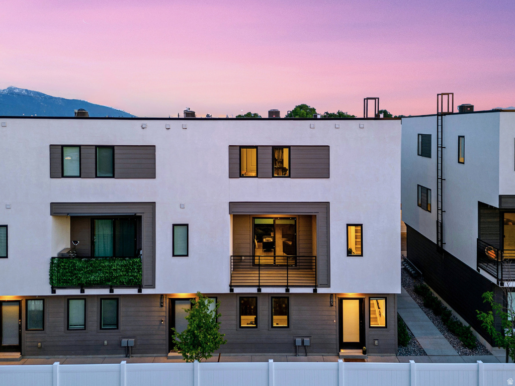 Modern architectural townhome featuring a private balcony with metal railings, a ground-level patio, and a white fence
