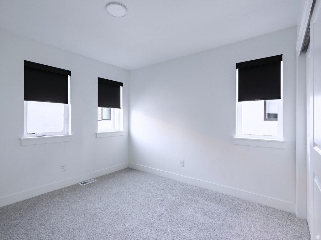 Bright room featuring three windows with roller shades, light grey carpeting, and white walls