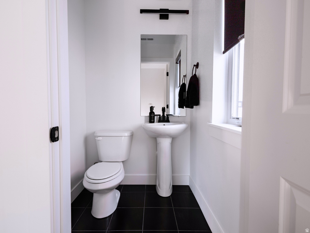 Powder room featuring a pedestal sink with a black faucet, a toilet, a window with a dark roller shade, and black square tile flooring