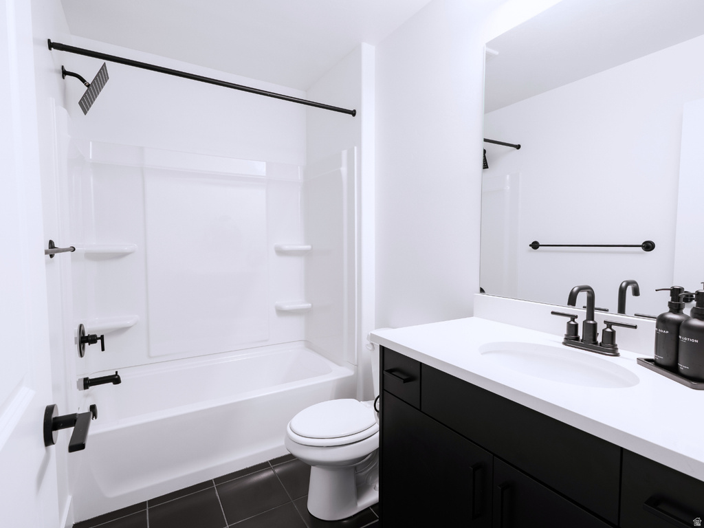 Bathroom featuring a white tub/shower combination, black shower fixtures, a white toilet, a dark vanity with a white countertop and integrated sink, and a framed mirror