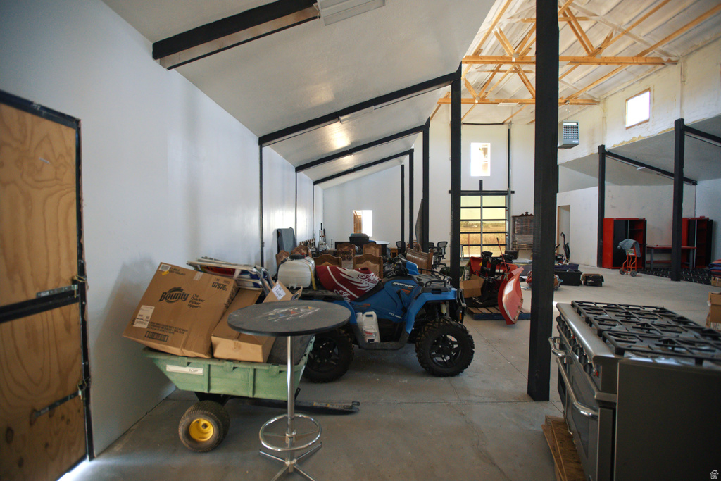 Spacious interior featuring a concrete floor, exposed wooden ceiling beams, multiple skylights, and a roll-up glass garage door