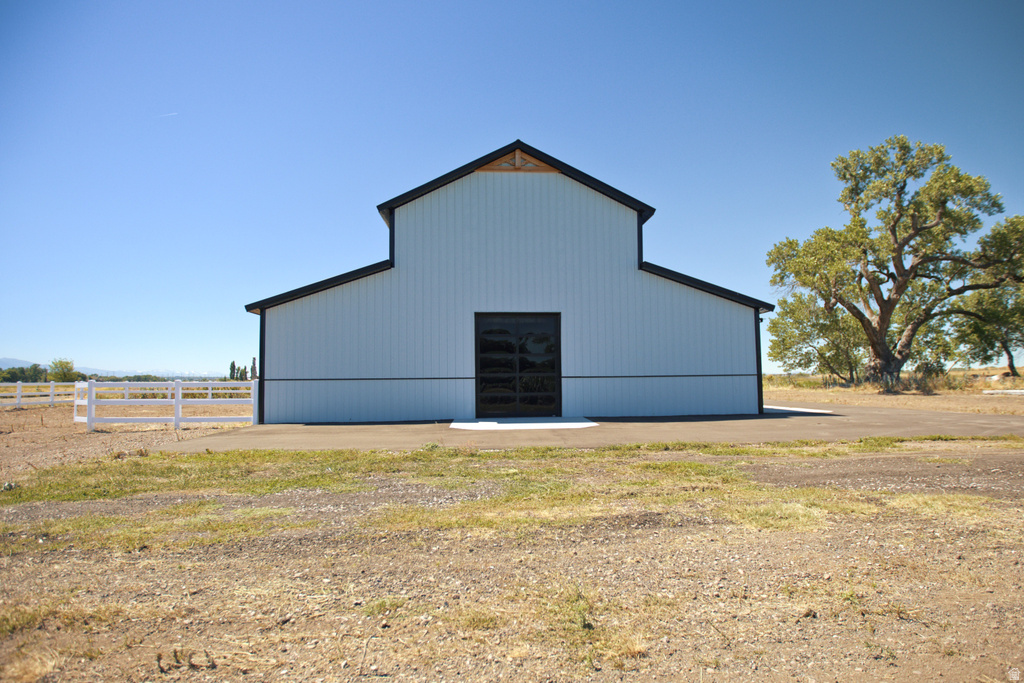 White-sided barn with black trim and a black garage door, set on a gravel and dirt lot