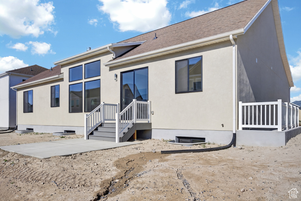 Rear exterior featuring a large concrete patio, a multi-pane picture window, and a sliding glass door with a deck