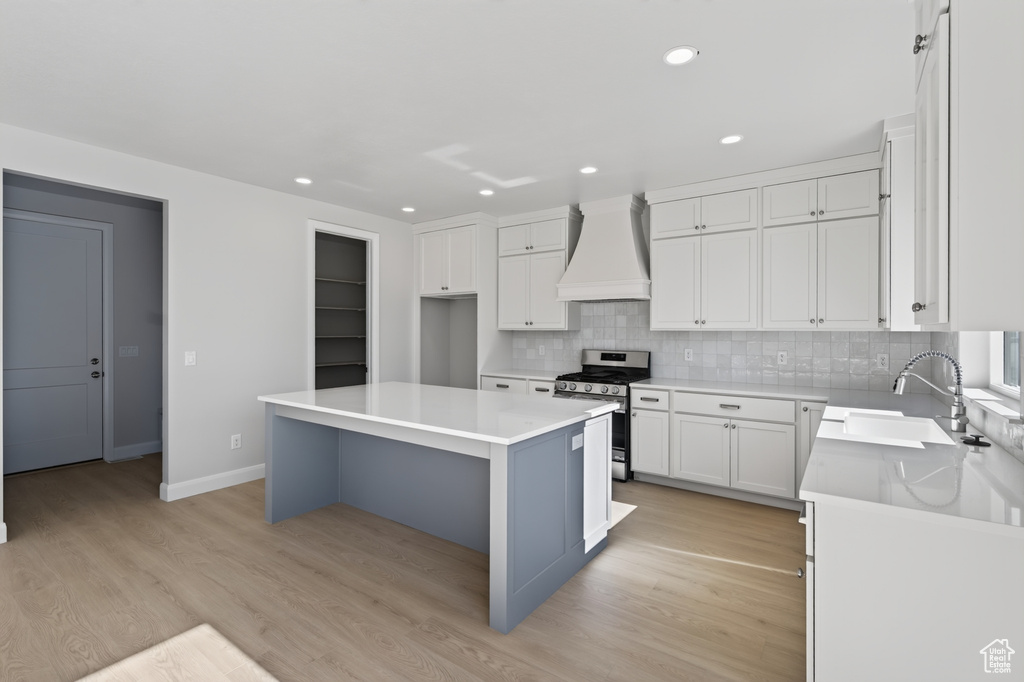 Modern kitchen featuring a central island with a solid surface countertop, white shaker-style cabinetry, stainless steel appliances, a tile backsplash, and light wood-finish flooring