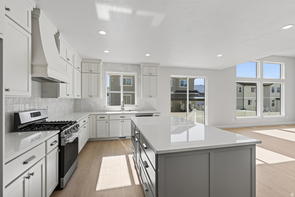 Spacious kitchen featuring white shaker cabinetry, stainless steel appliances, a large center island with a light-colored countertop, and light wood-finish flooring