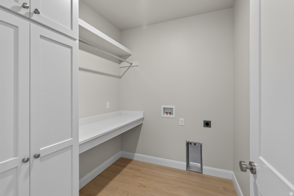 Laundry room featuring light wood-finish flooring, white built-in cabinetry with silver hardware, a white countertop, and a clothes hanging rod with shelving