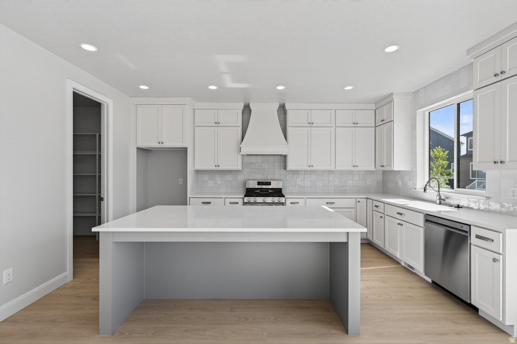 Contemporary kitchen featuring a spacious center island with a light-toned countertop, white shaker cabinetry, stainless steel appliances, and wood-finish flooring