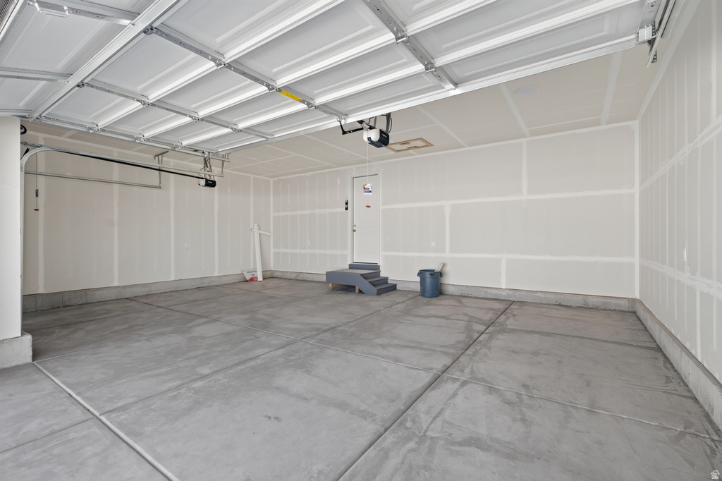 Spacious garage featuring a concrete floor, white drywall walls, an automatic garage door opener, and interior access via a white door with steps