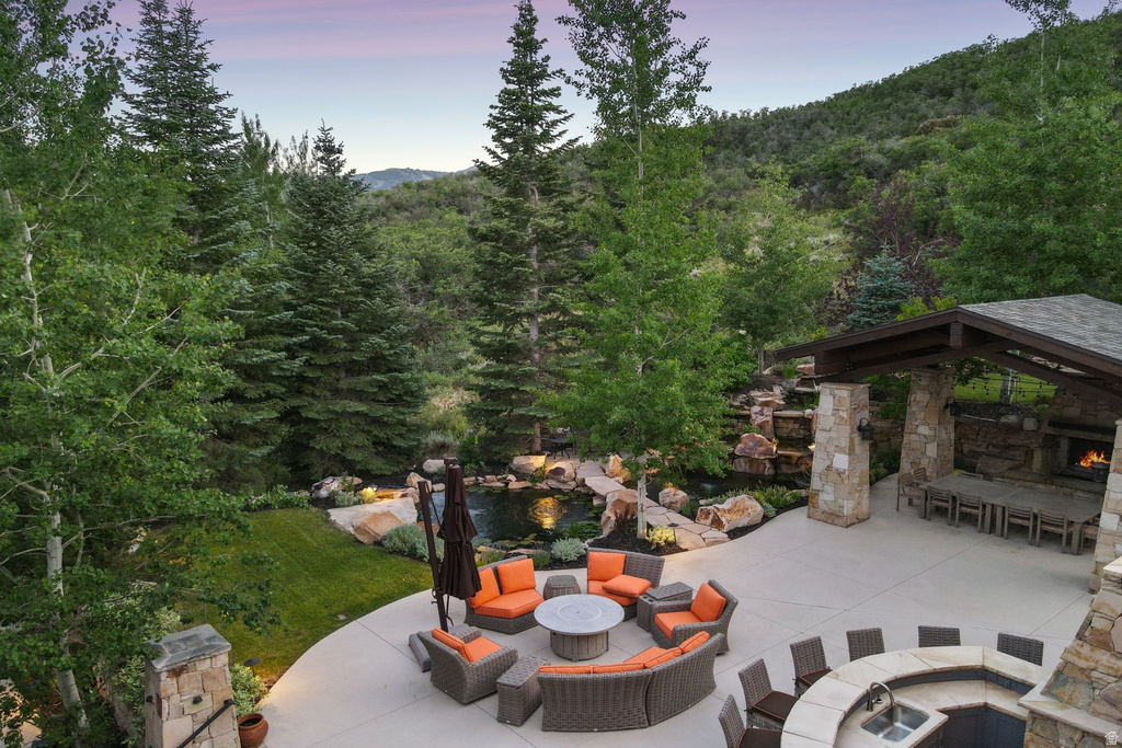Expansive outdoor living area featuring a stone fireplace, integrated outdoor kitchen with sink, and a multi-level water feature