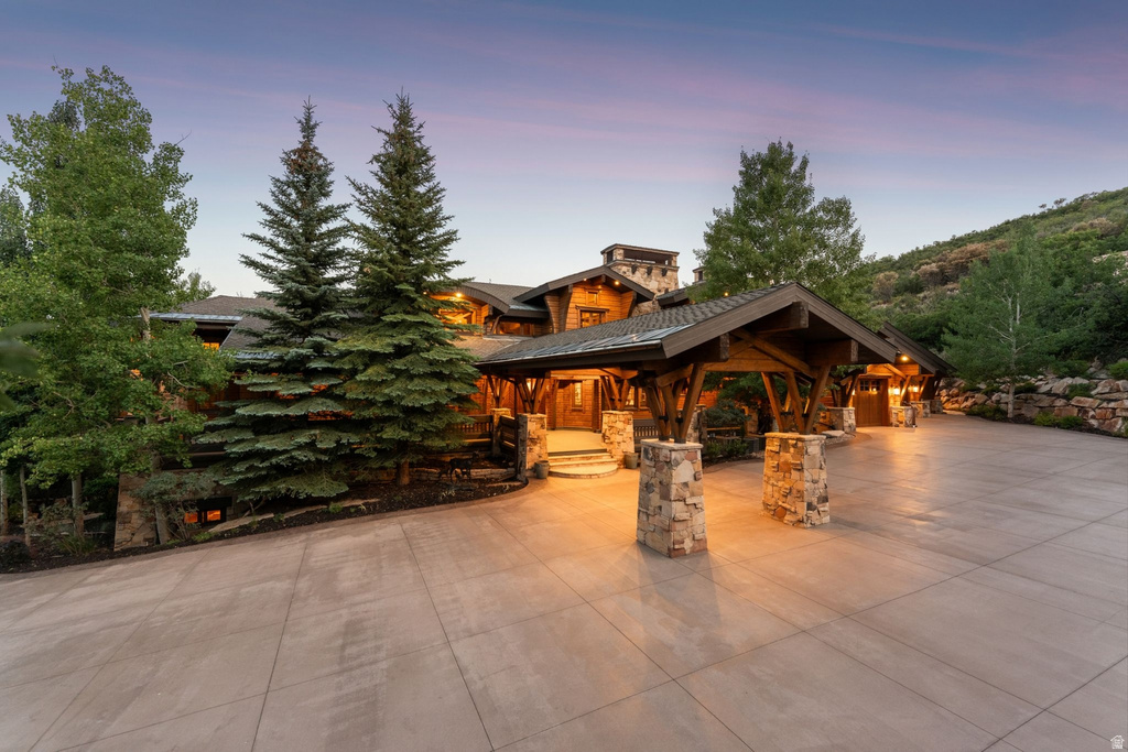 Stone and timber exterior featuring a porte-cochere entry, a substantial paved driveway, and established evergreens
