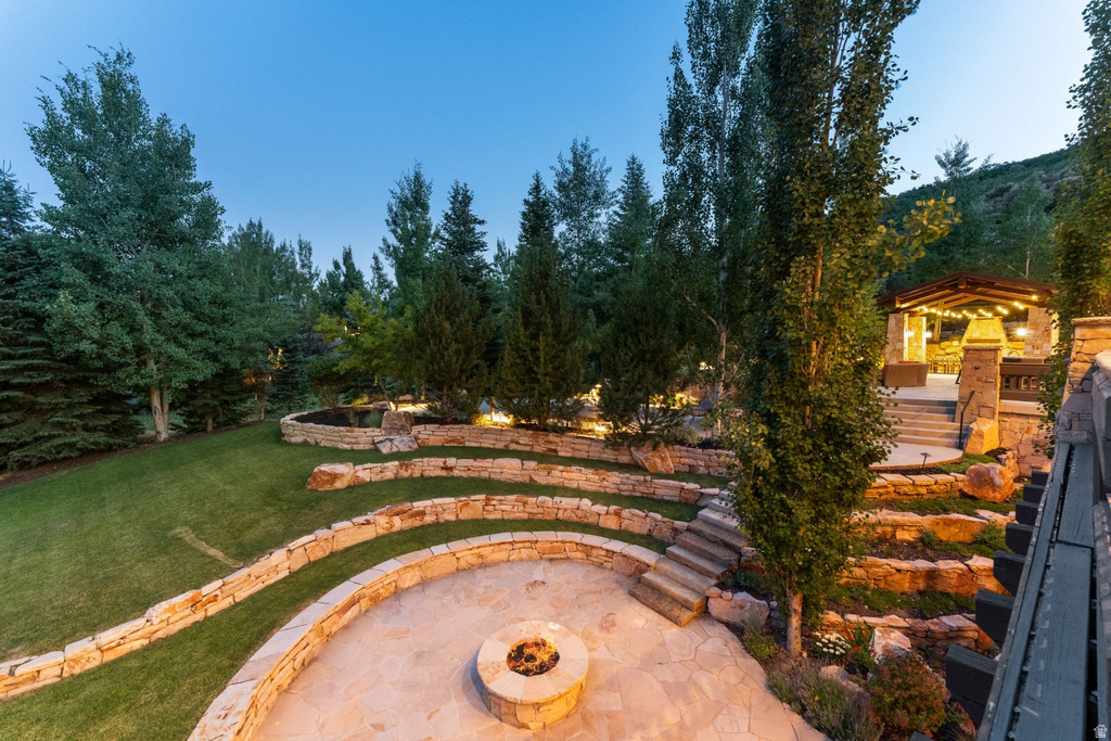 Terraced outdoor living space featuring a flagstone patio with a built-in fire pit, stone retaining walls, and a manicured lawn