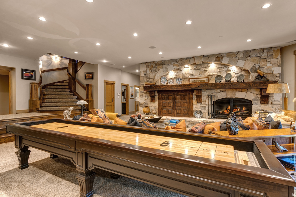 Spacious entertainment area featuring a stone fireplace with a substantial wood mantel, recessed lighting, a built-in shuffleboard table, and a carved wood spiral staircase