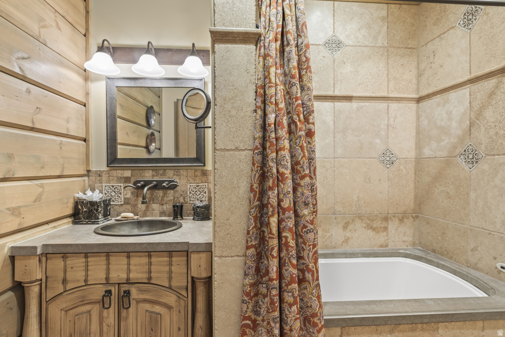 Bathroom featuring a built-in corner tub, light-toned tile surround with decorative accents, wood-finish vanity with a built-in sink, and wood plank wall paneling