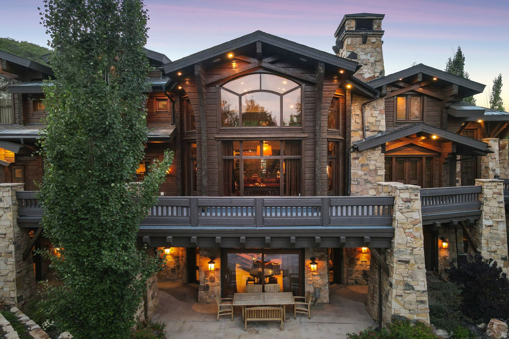 Multi-story wood and stone exterior featuring an expansive balcony, large arched window, and outdoor patio with built-in lighting