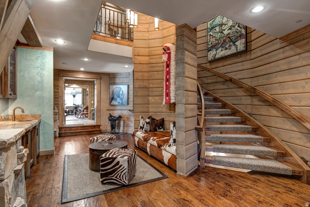 Curved staircase with carpeted treads, wood-finish flooring, wood-paneled walls, and a built-in wet bar with a stone countertop and copper-toned sink