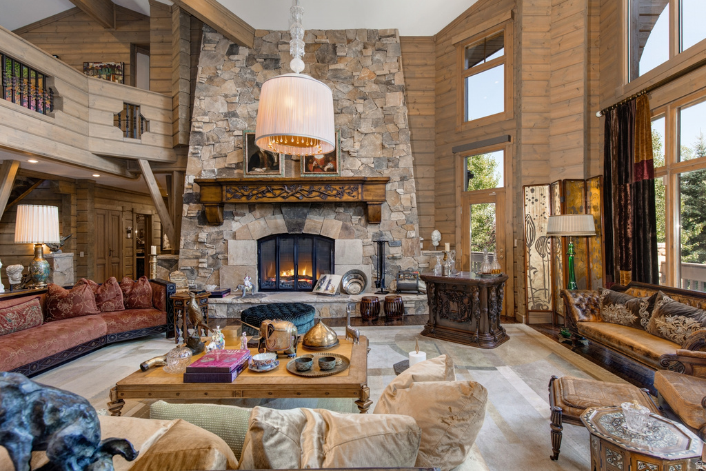 Spacious living area featuring a stone fireplace with a carved wood mantel, high wood-paneled ceilings, a second-story interior balcony, and large windows with exterior foliage