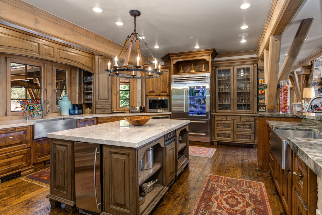 Gourmet kitchen featuring a substantial central island with integrated refrigeration, hardwood flooring, wood-finish cabinetry, stainless steel appliances, and stone countertops
