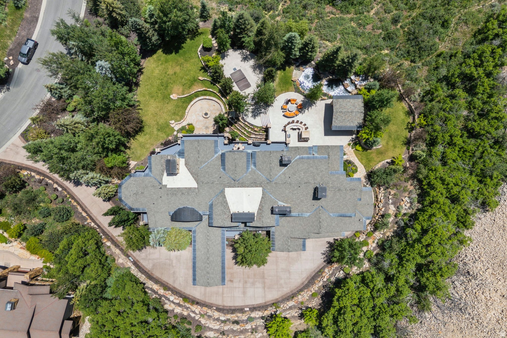 Expansive property featuring a multi-level structure with a complex roofline, extensive paved driveways, a large patio with built-in seating, and a dedicated fire pit area