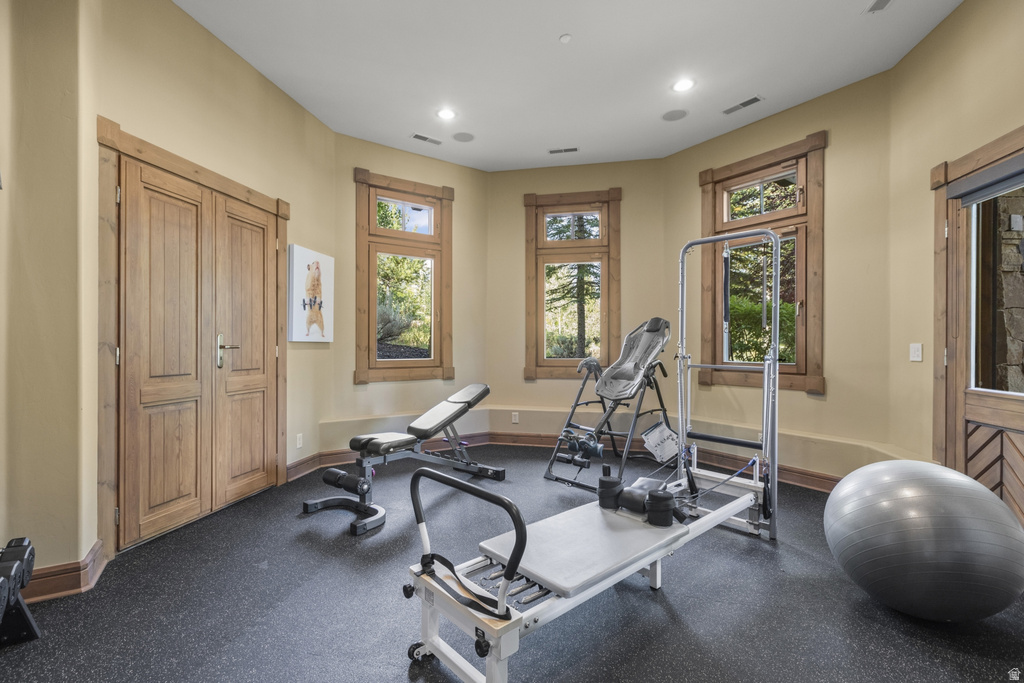 Dedicated fitness room featuring durable rubber flooring, recessed lighting, and multiple windows with natural wood trim
