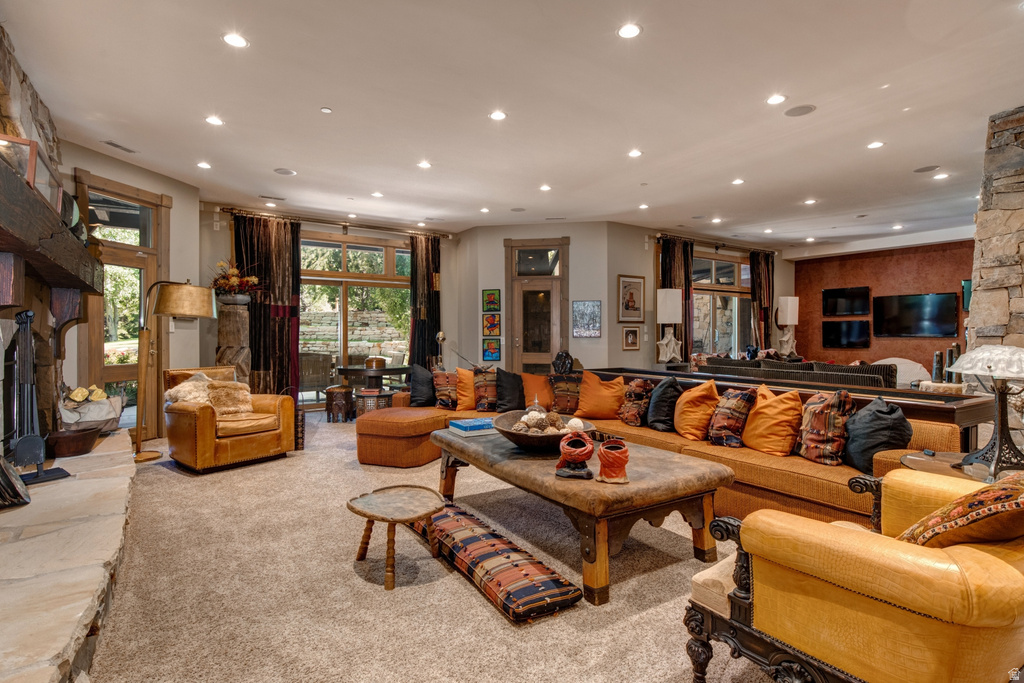 Spacious living area featuring a prominent stone fireplace, large windows, recessed lighting, wood-finish window frames, and soft carpet flooring