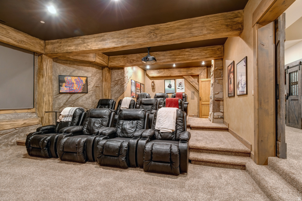 Dedicated media room featuring tiered seating, a large projection screen, rough-hewn timber beams, stone-finish walls, and plush carpeting