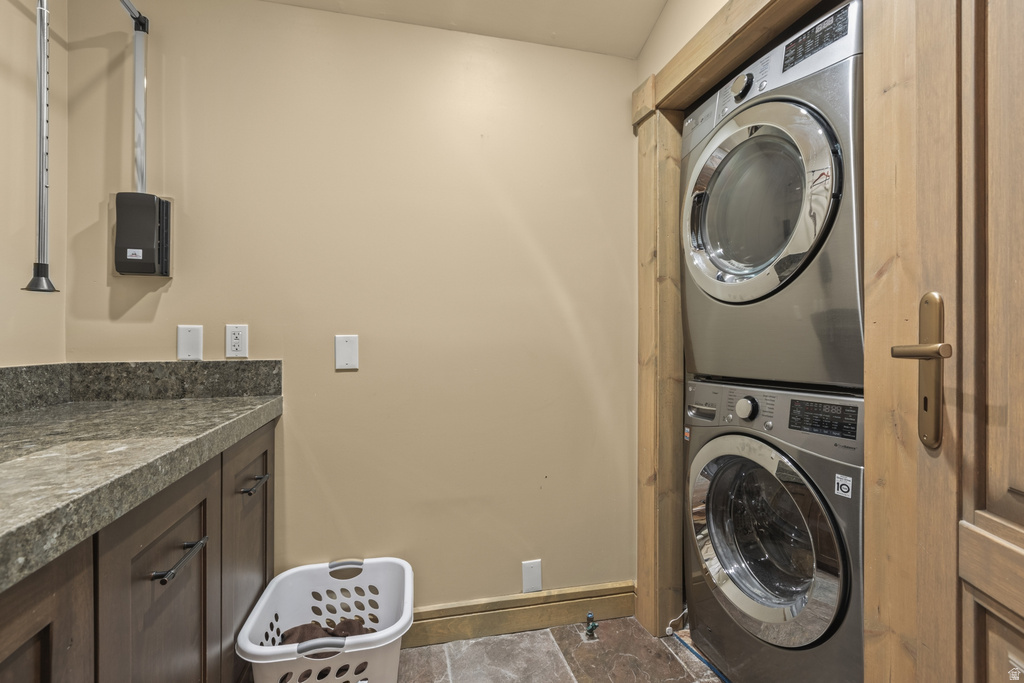 Laundry area featuring a stacked washer and dryer unit, built-in cabinetry with a stone-finish countertop, and stone tile flooring