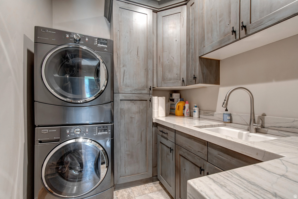 Laundry area with stacked appliances, light wood-finish cabinetry, and stone countertops featuring an undermount sink and gooseneck faucet