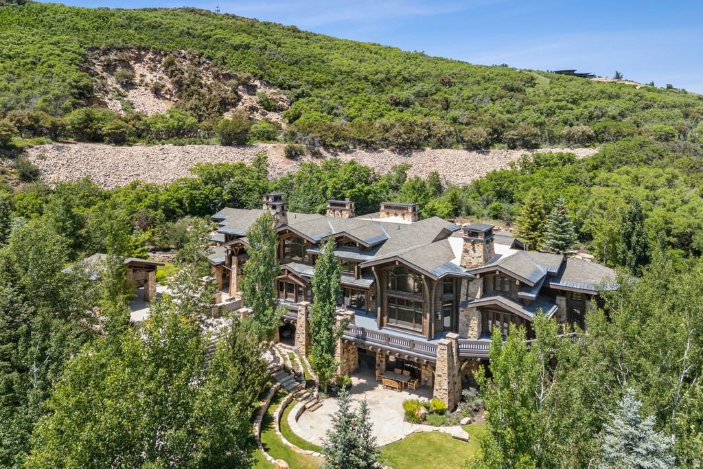 Expansive residence featuring a stone and wood facade, multiple balconies, a terraced lawn, and mature trees