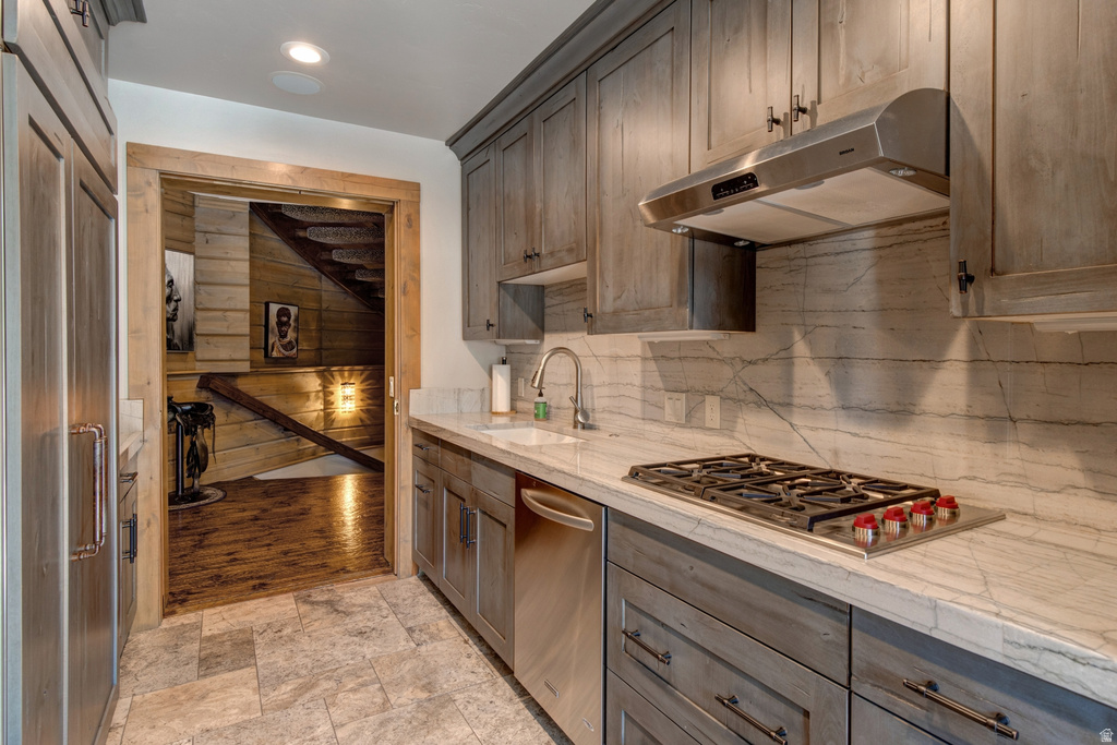 Kitchenette featuring a built-in gas cooktop, stainless steel range hood, stone slab countertops, a coordinating stone slab backsplash, and wood-finish cabinetry