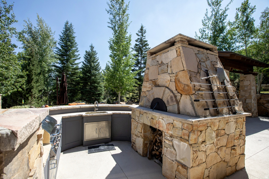 Outdoor kitchen featuring a built-in stone pizza oven with wood storage, a stainless steel grill, and an integrated sink