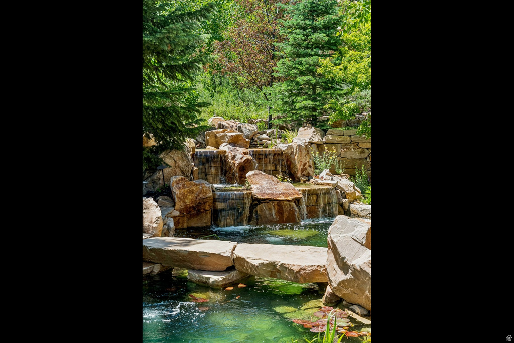Multi-tiered rock waterfall feature with a natural stone bridge spanning a tranquil pond