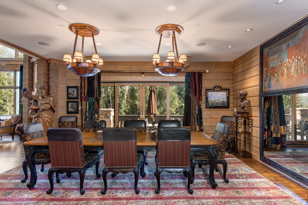 Dining area featuring wood plank walls, two ornate chandeliers, and a large dining table with six chairs