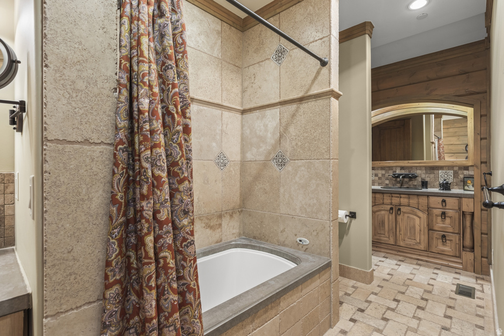 Bathroom featuring a tiled tub surround with decorative accents, an integrated bathtub, and a tiled floor