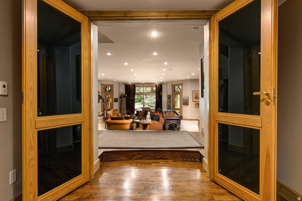 Hardwood flooring extends from the entry through French doors into a living area featuring recessed lighting and multiple windows