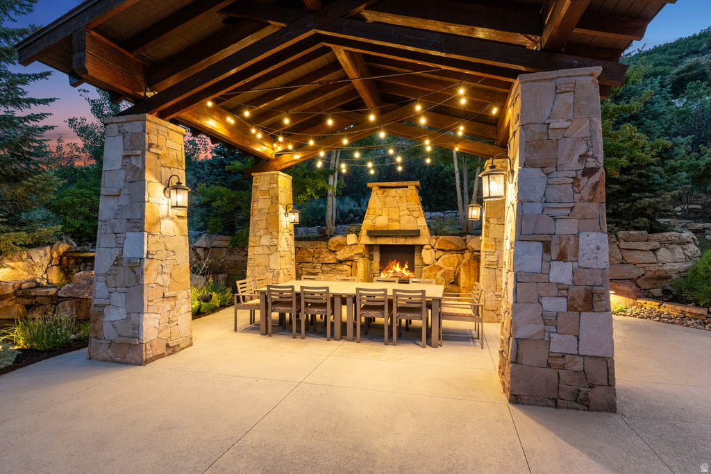 Covered outdoor patio featuring a stone-clad fireplace and stone pillars supporting a wood-beamed ceiling