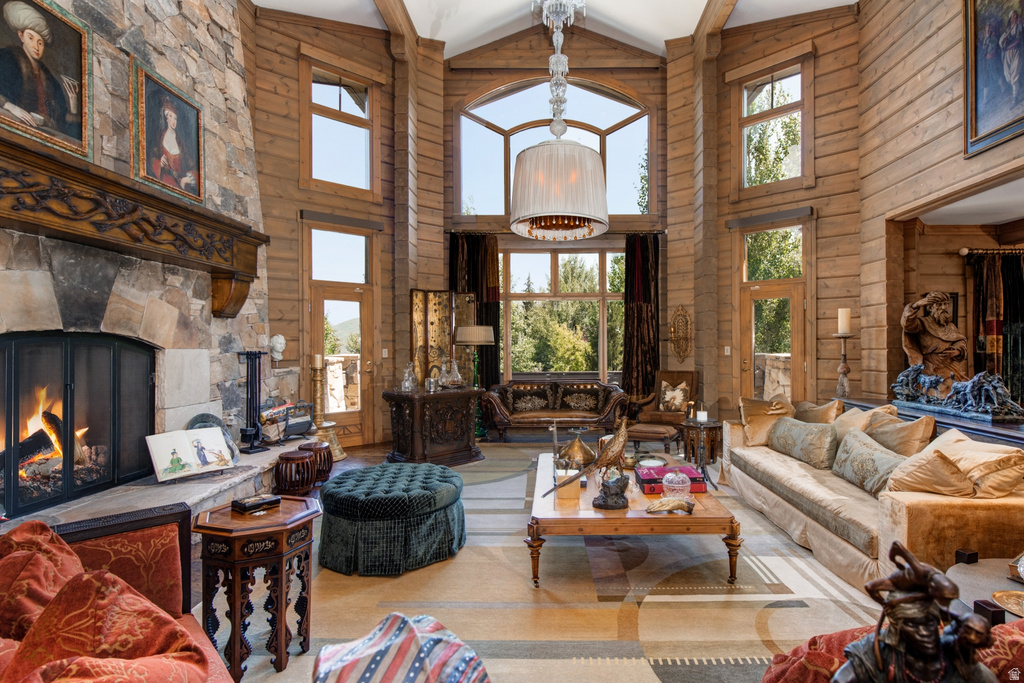 Grand living space featuring a two-story stone fireplace with an ornate wood mantel, natural wood paneling, floor-to-ceiling windows, soaring vaulted ceilings with exposed beams, and a large central chandelier