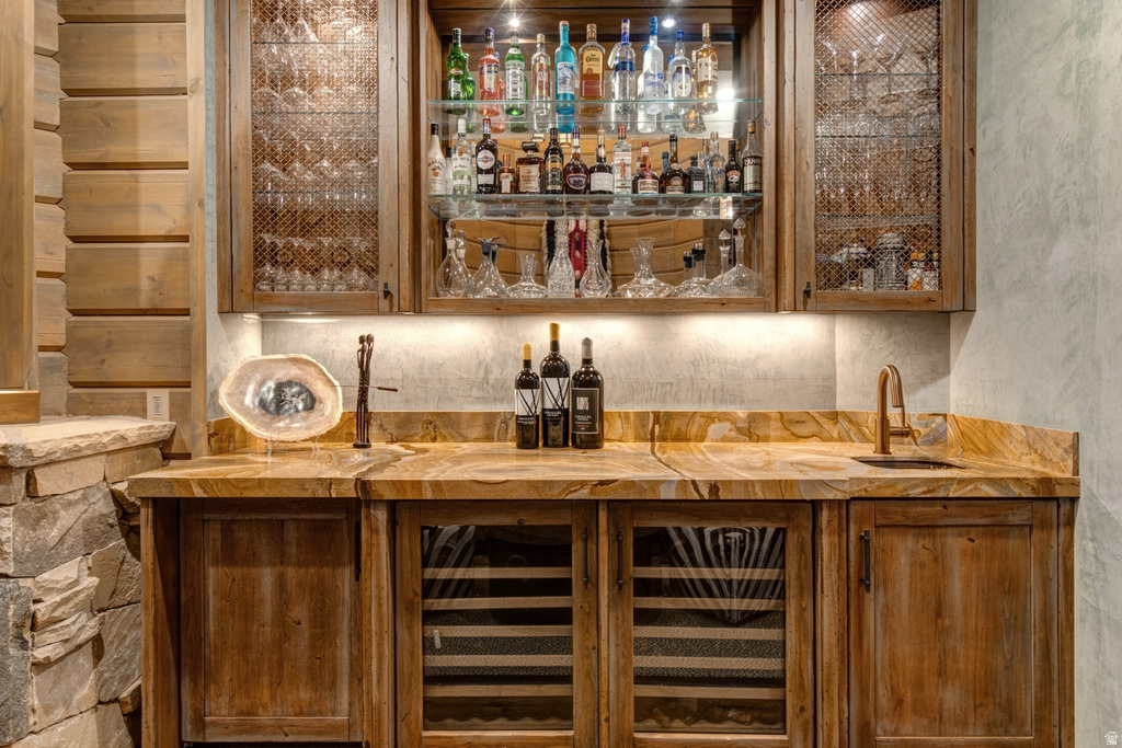 Custom bar area featuring richly veined stone countertops, a bronze-toned faucet with an undermount sink, and integrated wine refrigerators