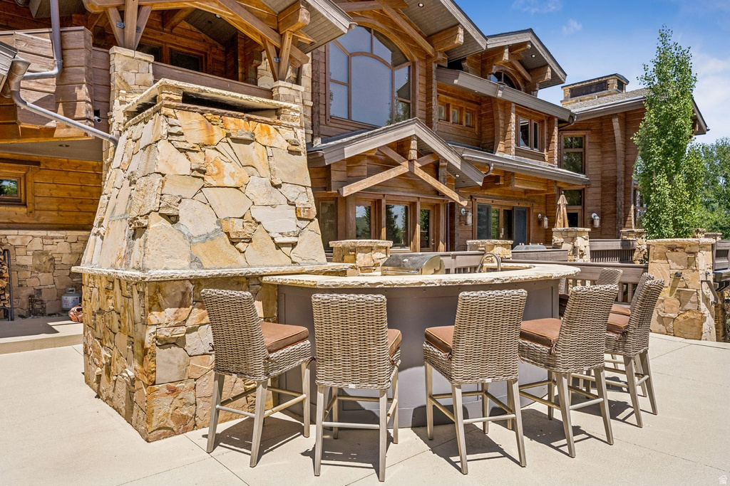 Outdoor kitchen featuring a built-in grill, sink, and stone-clad bar seating