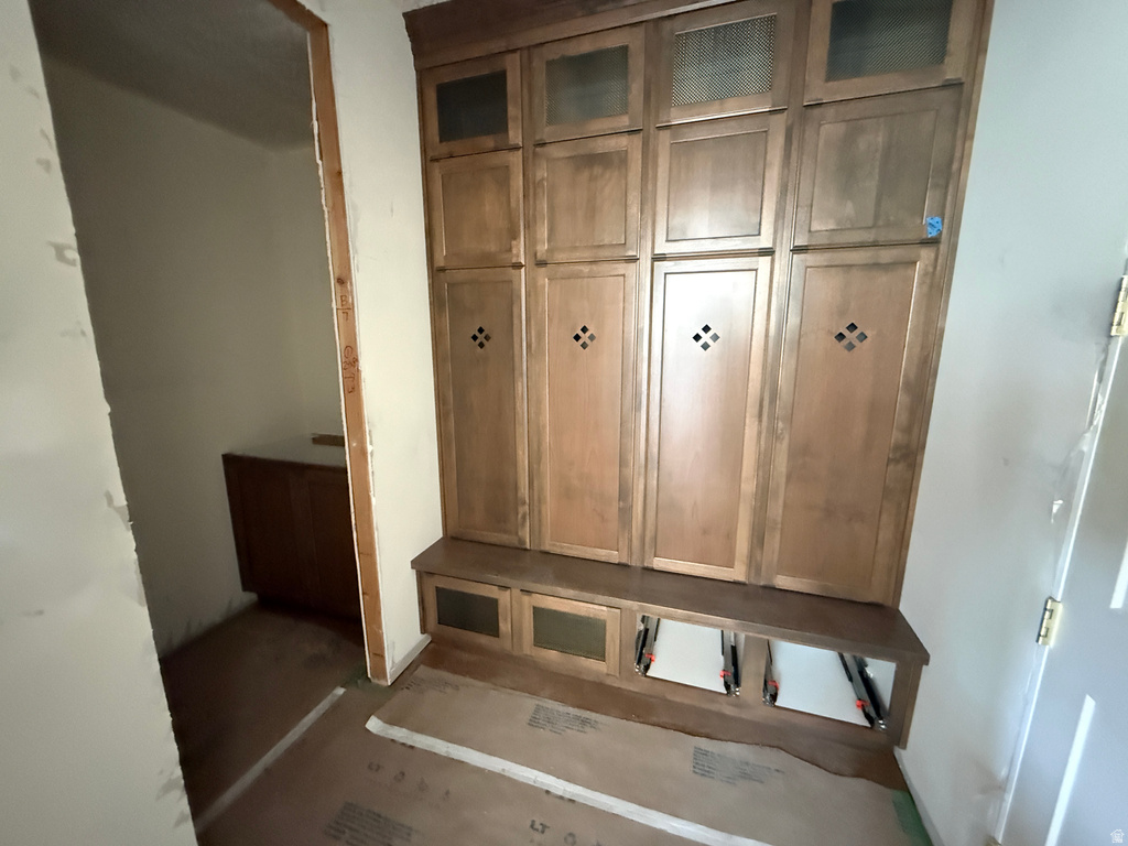 Entryway featuring custom wood cabinetry with glass-panel upper doors and decorative hardware, complemented by a built-in wood bench with storage cubbies and a wood-finish flooring base