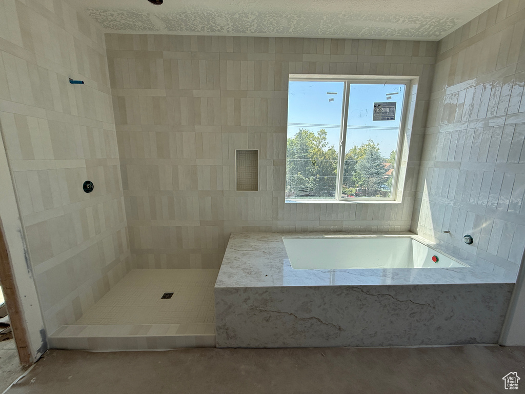 Spa-inspired primary bathroom featuring a spacious walk-in shower with linear tile detailing, a freestanding soakable bathtub with polished stone surround, dual vanity setup with quartz countertops, recessed lighting, and abundant natural light from overs