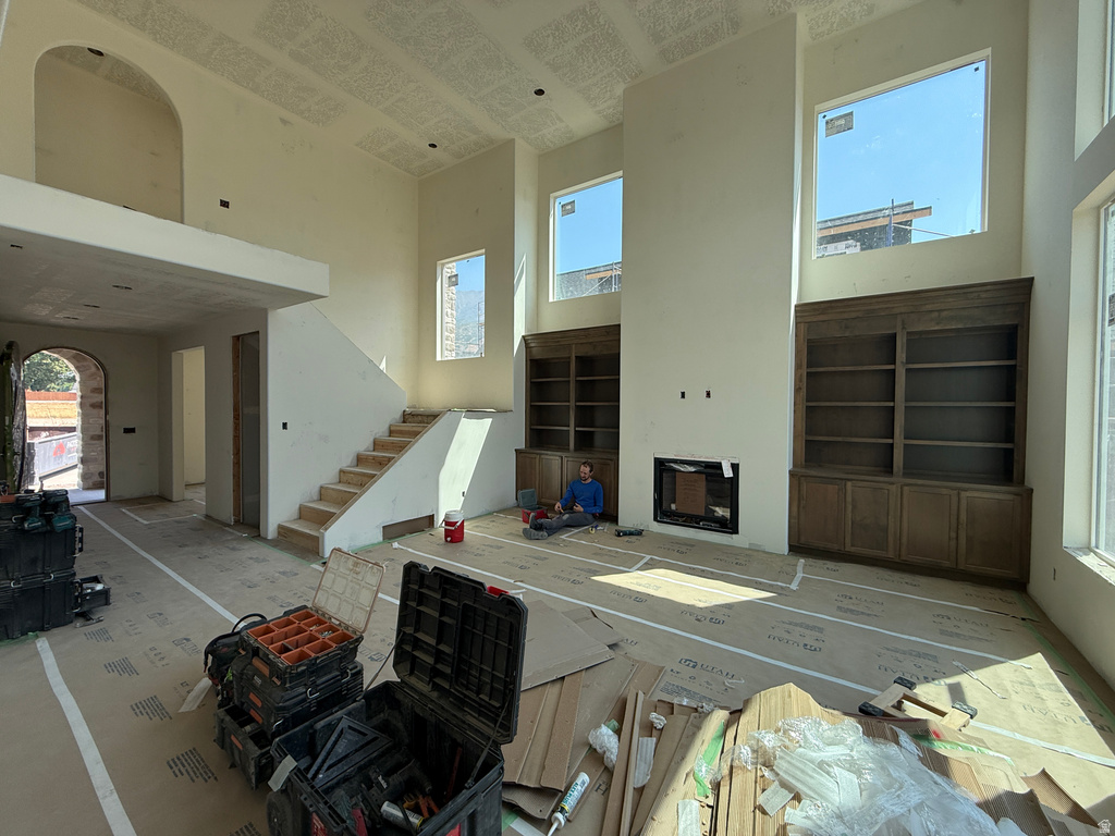 Soaring two-story great room with abundant natural light from multiple high-set windows, exposed ceiling detail, and substantial floor-to-ceiling built-in cabinetry